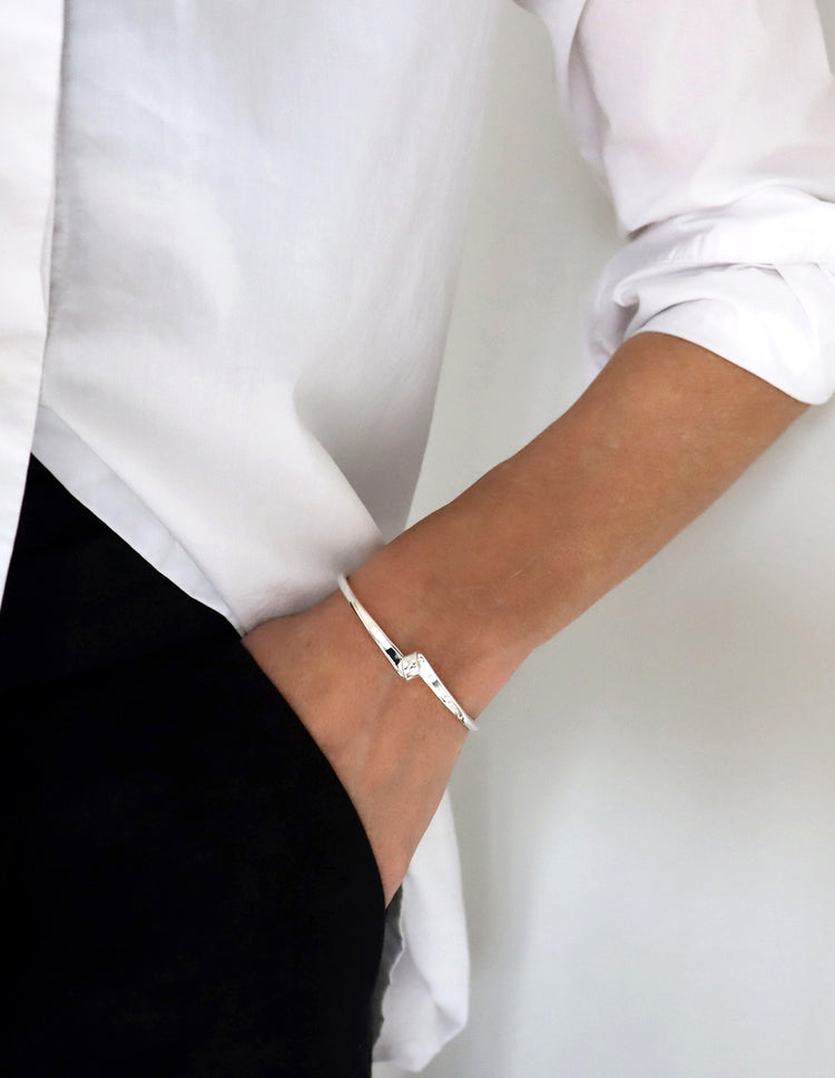 Kvinnan som bär ett smalt stelt silverarmband till vit skjorta och svarta byxor.