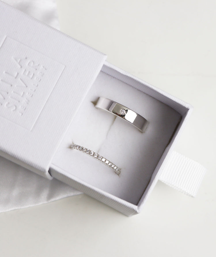 Ett set med vigsel/förlovningsringar i silver med diamanter. Ringarna presenteras i en vit ringask.