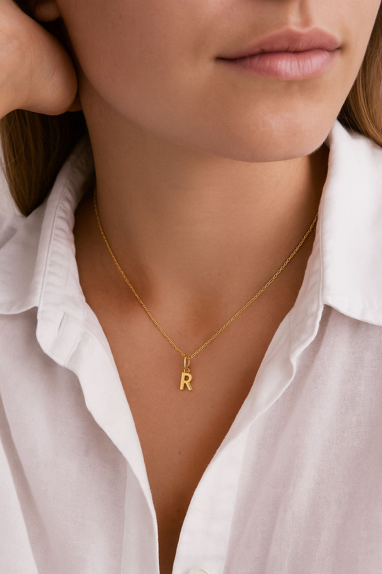 Kvinna i vit skjorta som bÀr ett bokstavshalsband i guld.