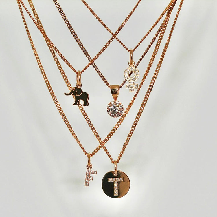 Flera guldhalsband som hänger i lager på lager med små berlocker med olika motiv. Berlocker i guld med diamantbokstav och andra guldberlocker.