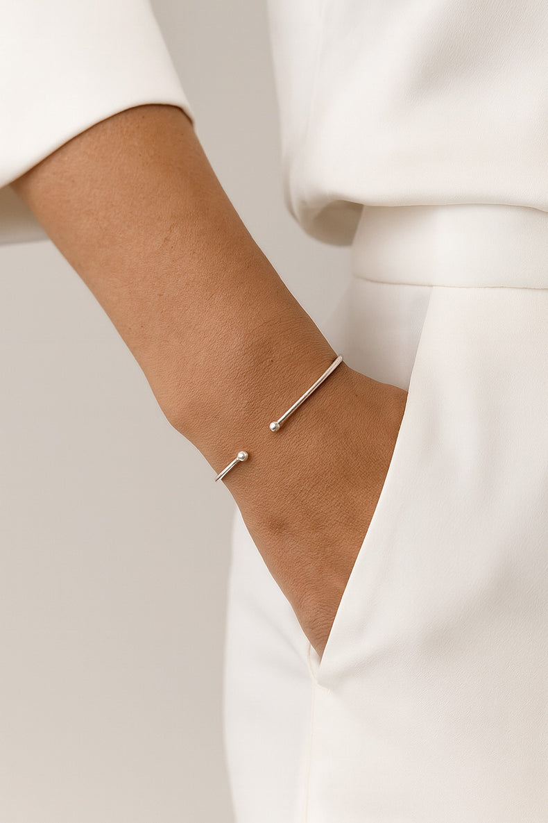 Tunt stelt silverarmband med små kulor, bärs av kvinna klädd i vit kostym.