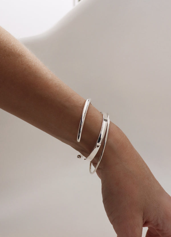 Tjej som bär flera stela armband i silver i kombination.