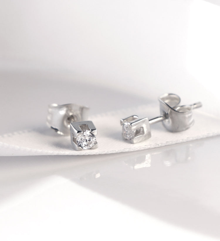 Örhängen i silver med diamanter som ligger på ett vitt tyg band.