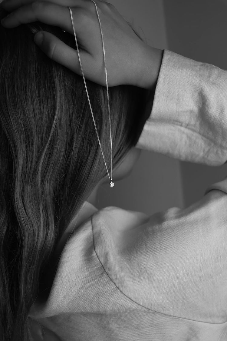 En tjej som hÄller ett diamanthalsband i handen med en liten gnistrande diamant.