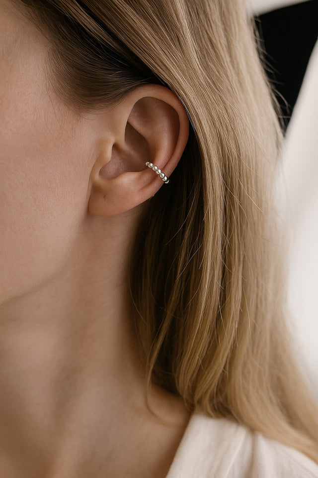 tjej som bär ett ensamt örhängen en bit upp på örat. en ear cuff i silver med små silverkulor.
