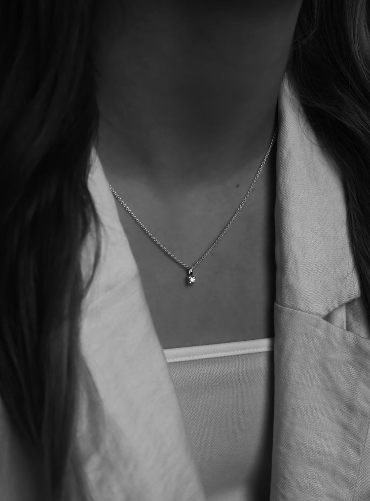 Svart-vit bild på en tjej som bär ett kort diamanthalsband med berlock i kedja.