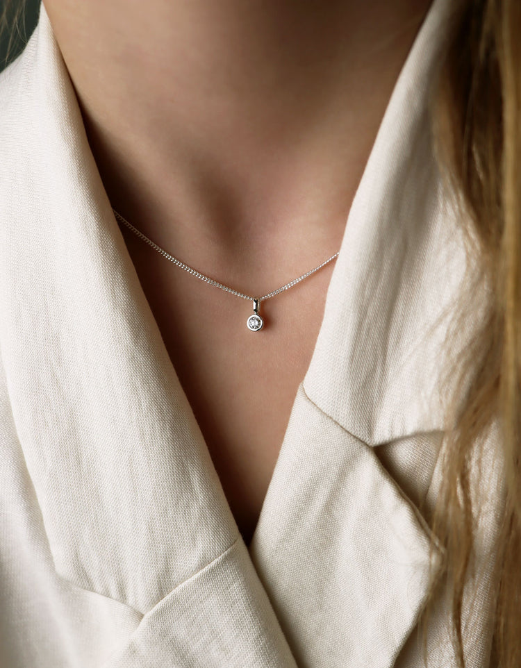 Diamanthalsband med hÀngsmycke och kedjan som bÀrs högt upp i halsen. Kvinnan bÀr vit kavaj.