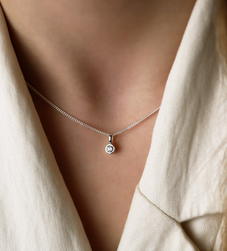 Tjej som bÀr ett halsband med diamantberlock i silverkedja.