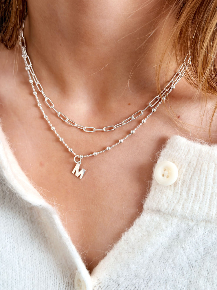 Tjej som bÀr ett kort kedjehalsband med Paperclip kedja kombinerat med ett bokstavshalsband.