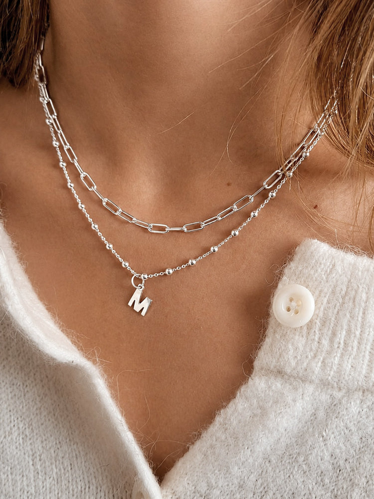 Tjej som bär två silverhalsband. Paperclip kedja och bokstavshalsband.