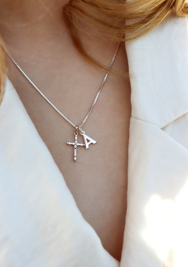 Tjej som bär ett silverhalsband med silverkors och bokstavsberlock.