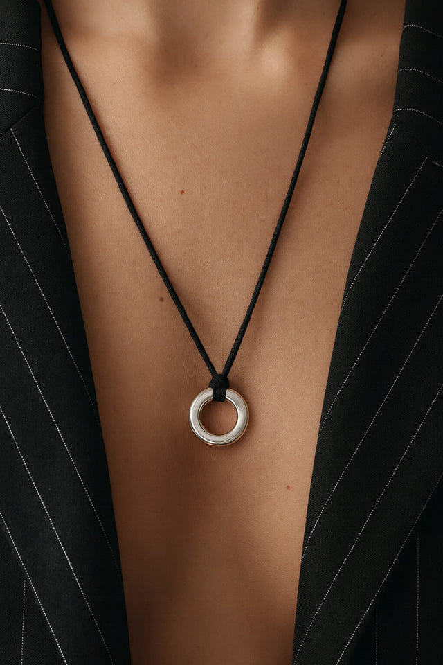 Kvinna som bär ett halsband med ring i silver i svart läderband. Hon bär en svart kavaj med djup urringning.