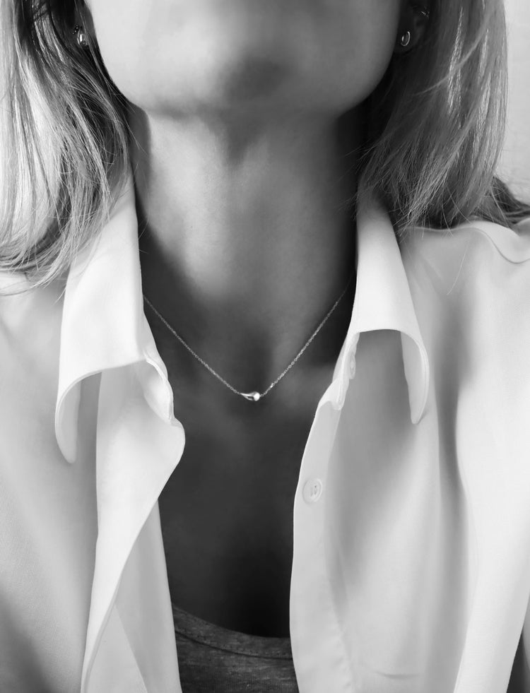tjej som bär ett kort tunt silverhalsband med droppe