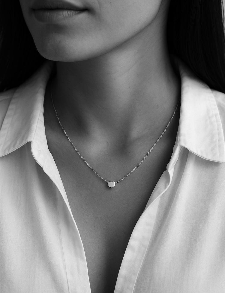 Kvinna som bär ett kort silverhalsband med ett litet silverhjärta. Hon har uppknäppt vit skjorta.