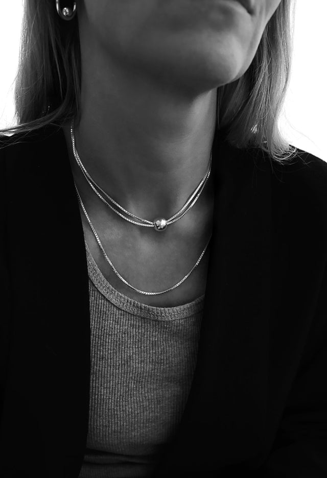 En tjej som bär två silverhalsband. Ett kort halsband med kedja virad två varv kombinerat med en längre silverkedja.