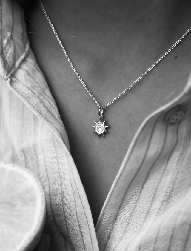 Tjej som bär ett halsband i silver med en berlock av sol.