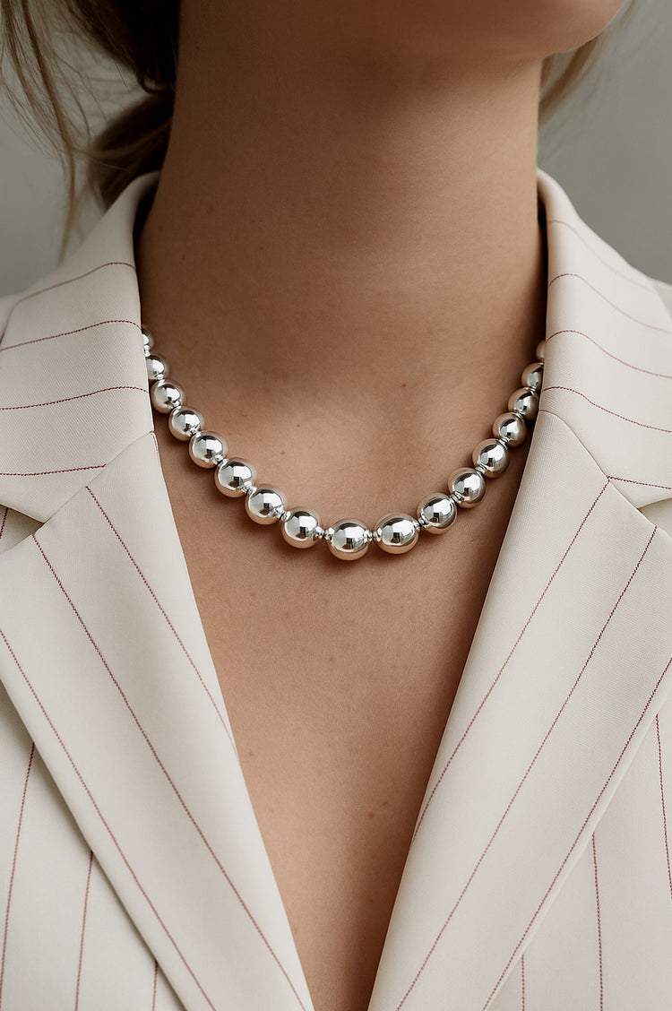 tjej som bär ett stort silverhalsband med stora silverkulor till vit kavaj .