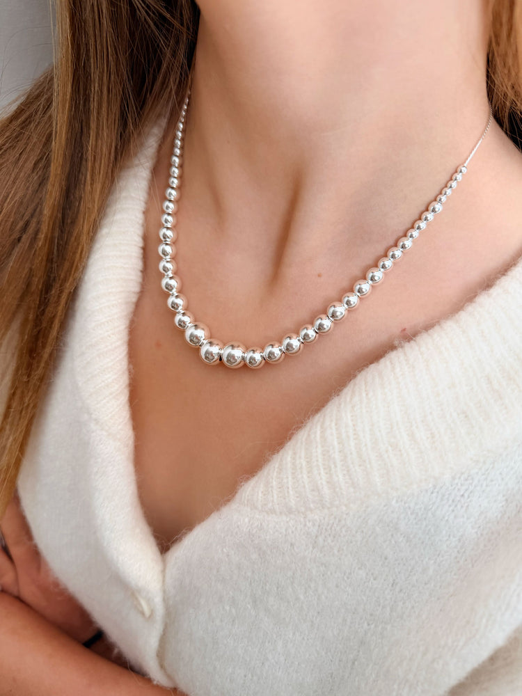 Tjej som bär ett silverhalsband med silverkulor i olika storlekar som är trädda på en silvervajer.