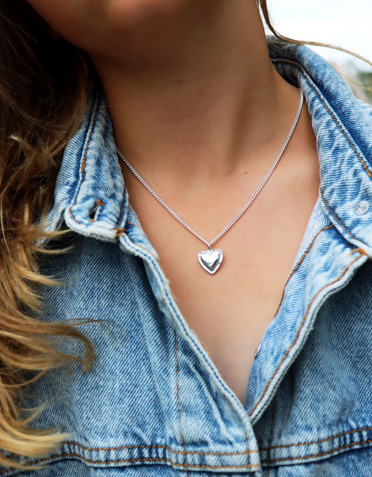 Tjej som bär ett halsband med silverhjärta i pansarkedja.