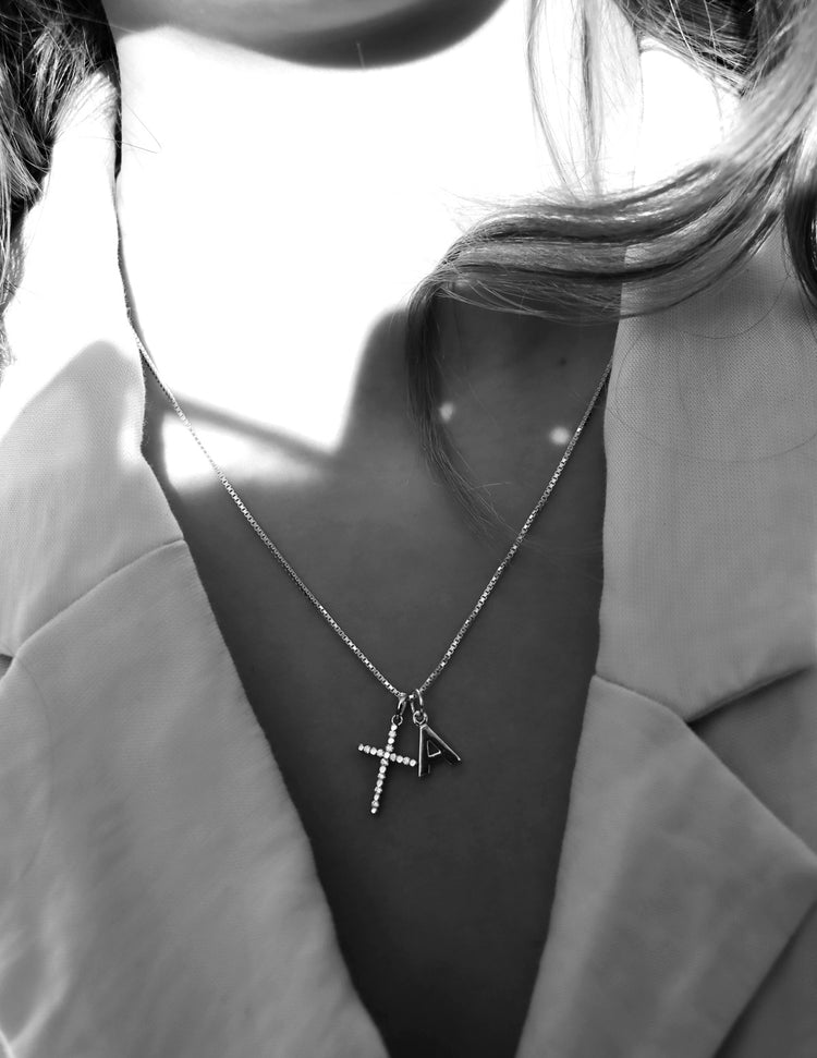 Tjej som bär ett silverhalsband med silverkors och bokstavsberlock.