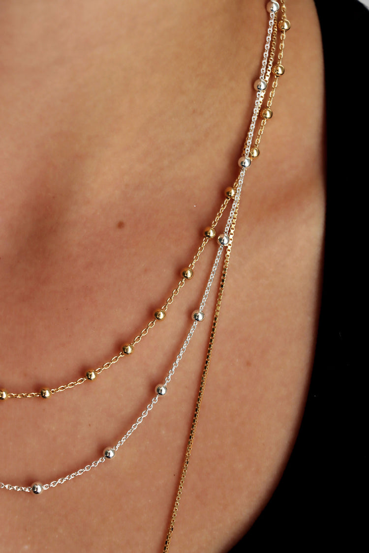 Tjej som bär ett kort guldhalsband med tunn kedja och små kulor kombinerat med en silverkedja.