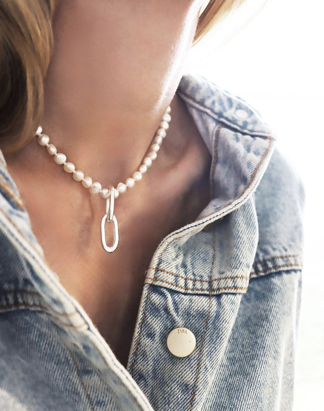 Tjej i jeansjacka som bär ett kort pärlhalsband som har två ovala silverlänkar som hängsmycke.