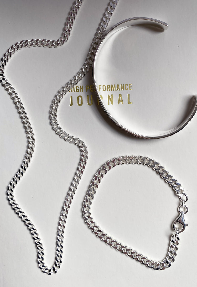 Halsband och armband med pansarkedjor placerade på en bok med texten High Performance Journal.