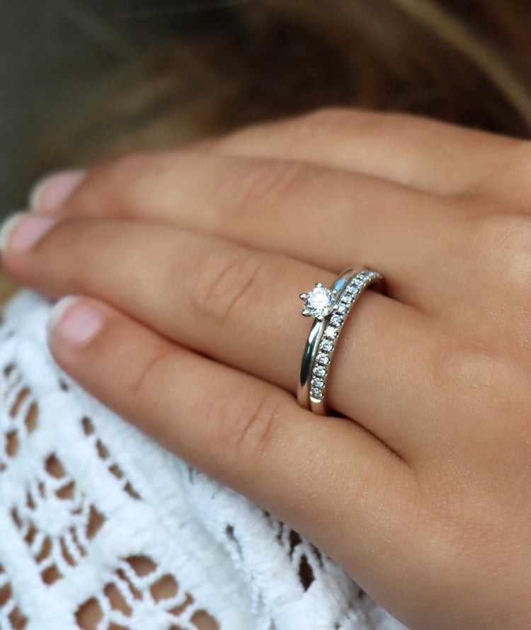 Tjej som bär två diamantringar som vigsel- och förlovningsring. Silverringar med diamanter. En alliansring med flera små diamanter och en ring med en diamant 0,25 ct.