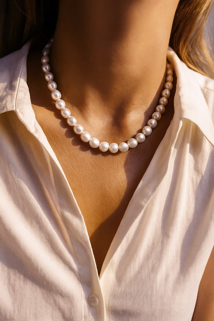 Kvinna som bärett somrigt pärlhalsband med vita barockpärlor till vit skjorta.