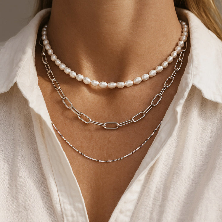 tjej som bär flera halsband i olika längder. Ett pärlhalsband, ett halsband med kedja och en tunn silverkedja.