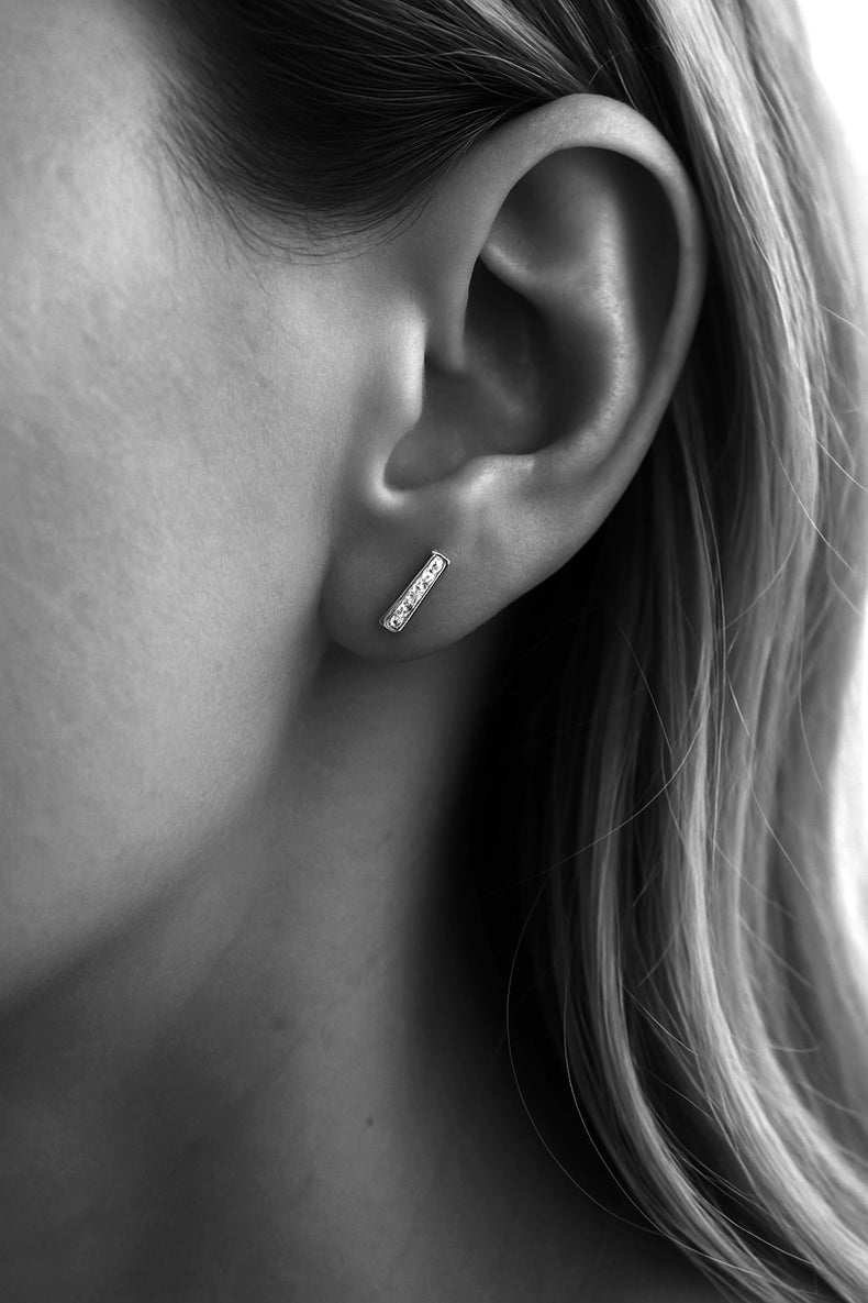 Kvinna som bär diamantörhängen met stavar i silver som är infattade med sex små diamanter.