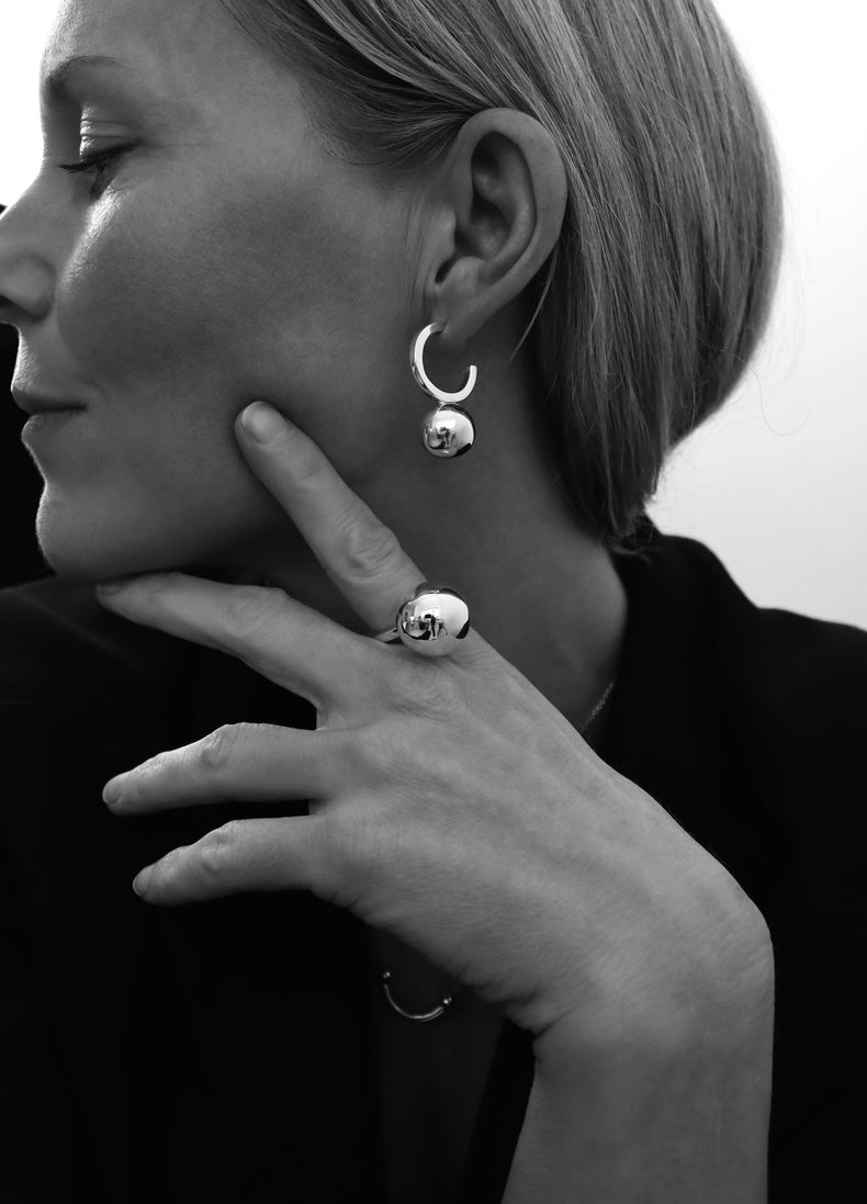 Tjej som bär ett stort silverörhänge med en stor silverkula i en hoop ring. Hon bär en matchande silverring med en stor kula.
