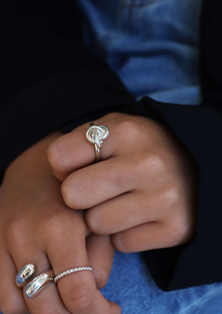 Tjej som bär en silverring med knut på pekfingret, kombinerat med flera andra silverringar på andra handen.