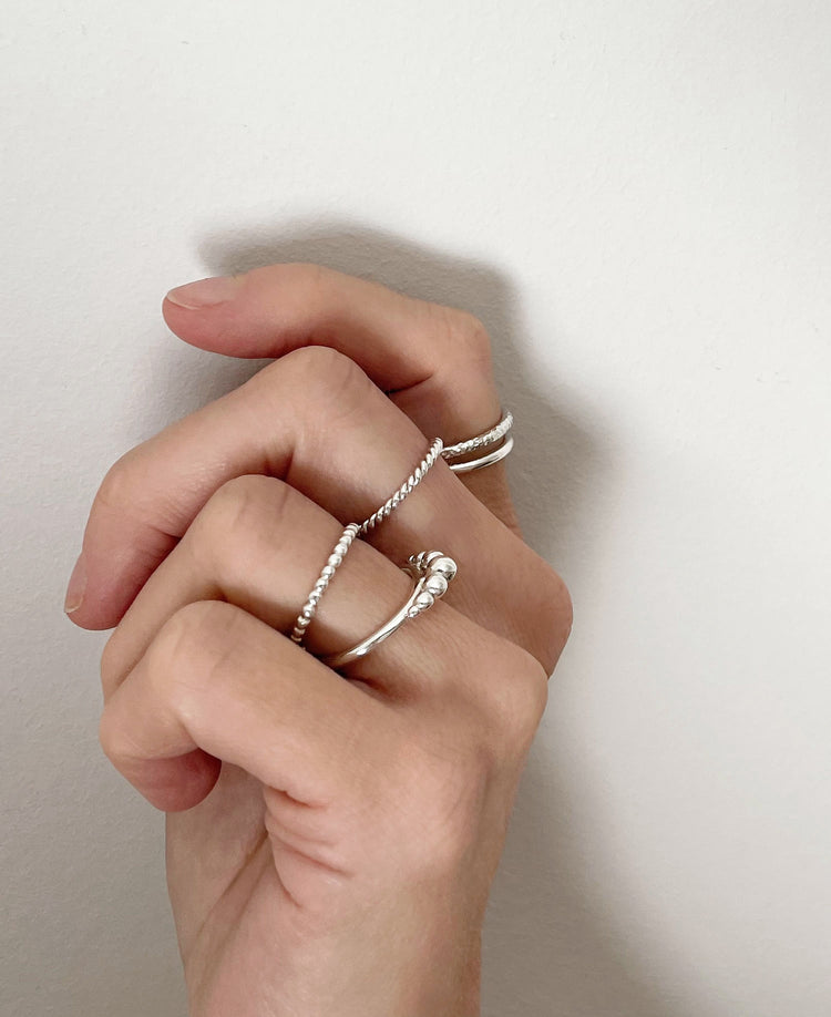 Flera smala silverringar som bärs i kombination på flera fingrar.
