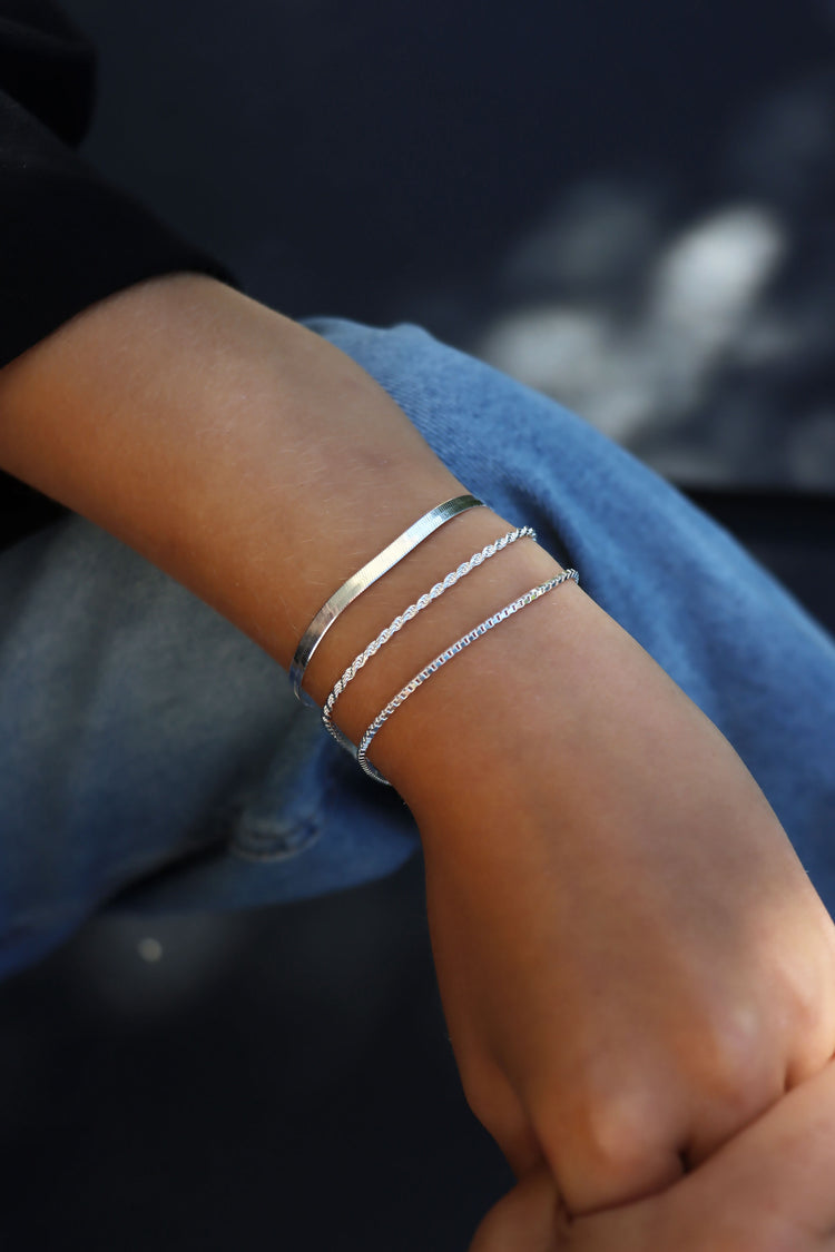 Tjej som bÀr tre smala silverarmband i kombination. Rope kedja, Box kedja och Snake kedja.