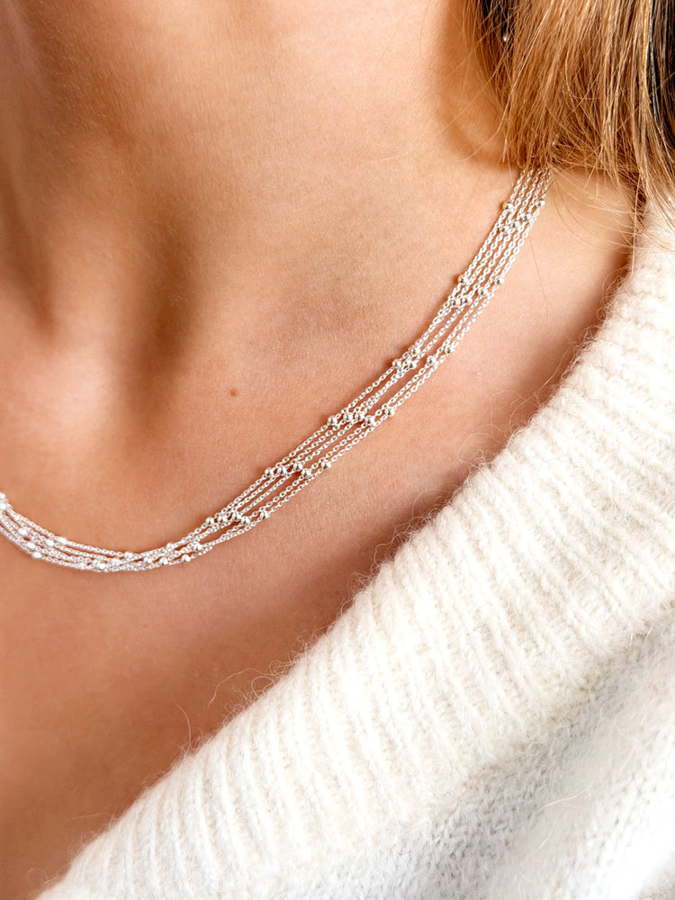 Tjej som bär ett kort halsband i silver med tunna kedjor och små silverkulor.