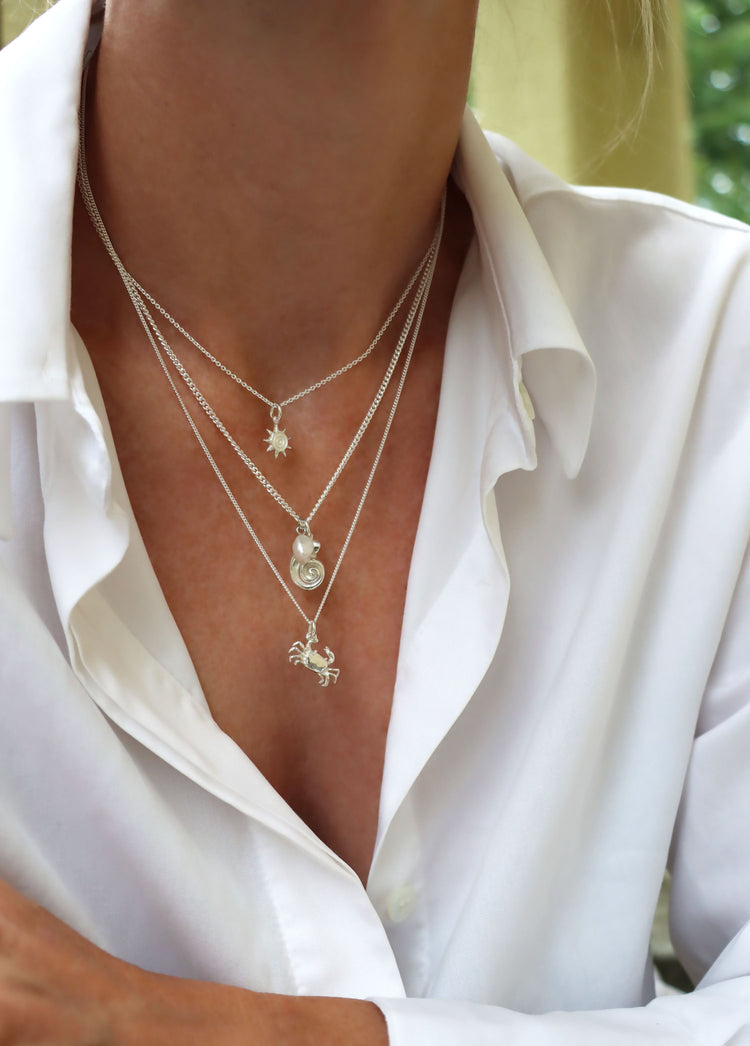 Kvinna som bÀr tre silverhalsband i olika lÀngder. En liten sol, en snÀcka och en krabba i silver.