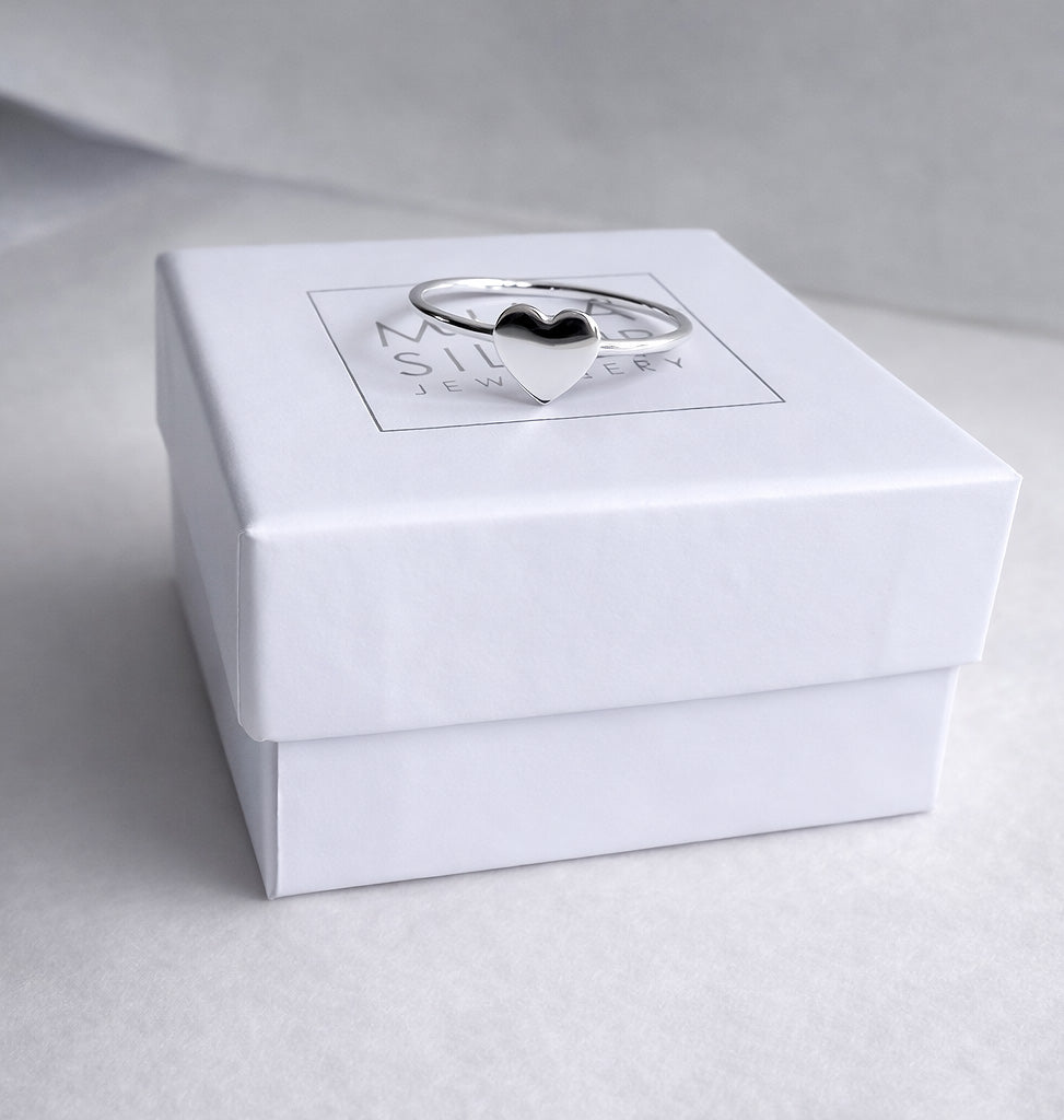 En ring i silver med ett hjÀrta placerad pÄ en vit ask frÄn Mila Silver.