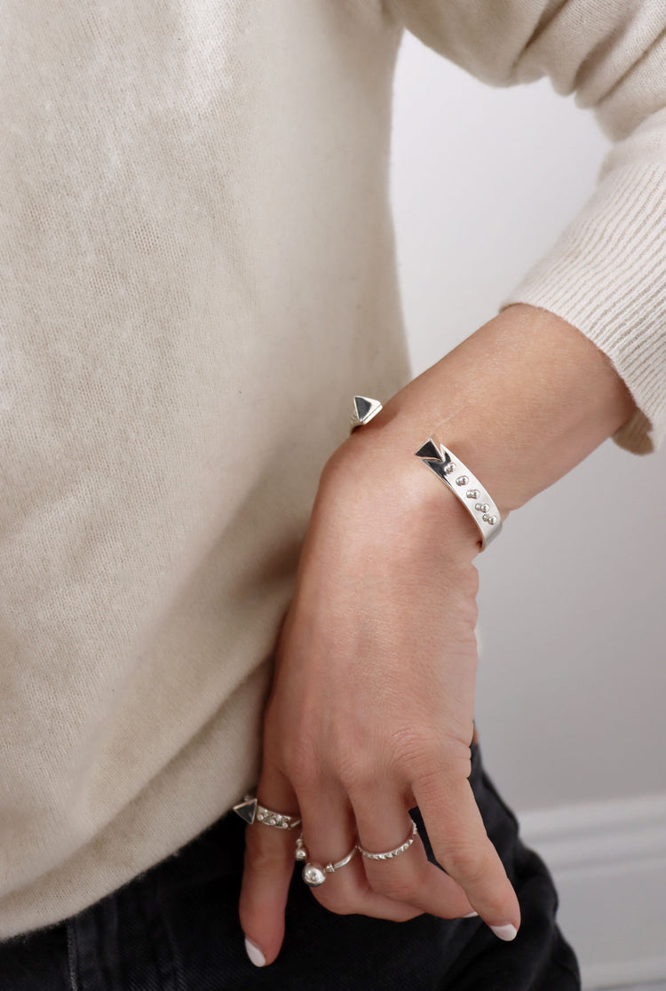 Tjej som bär ett stelt silverarmband med matchande silverringar.