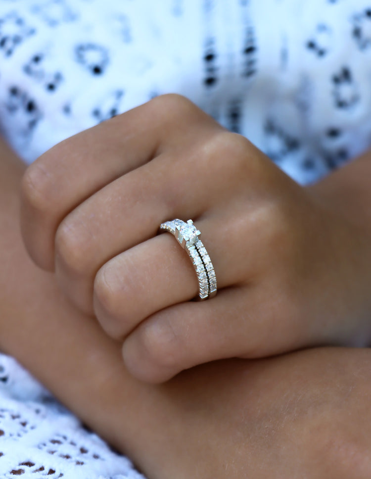 Tjej som bär ett set med vigsel och förlovningsringar med diamanter. Ringarna är täckta med små diamanter runt om ringarna. Den ena ringen har en stor diamant i mitten med boxformat fattning som sticker upp.