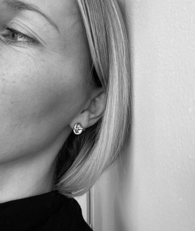 Kvinna bär silverörhängen med knutar som sitter fast på örat.