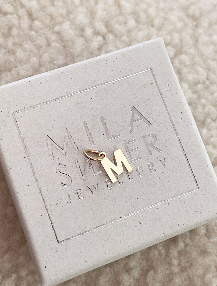 HÀnge med utstansad BOKSTAVSBERLOCK i guld placerad pÄ present-ask.