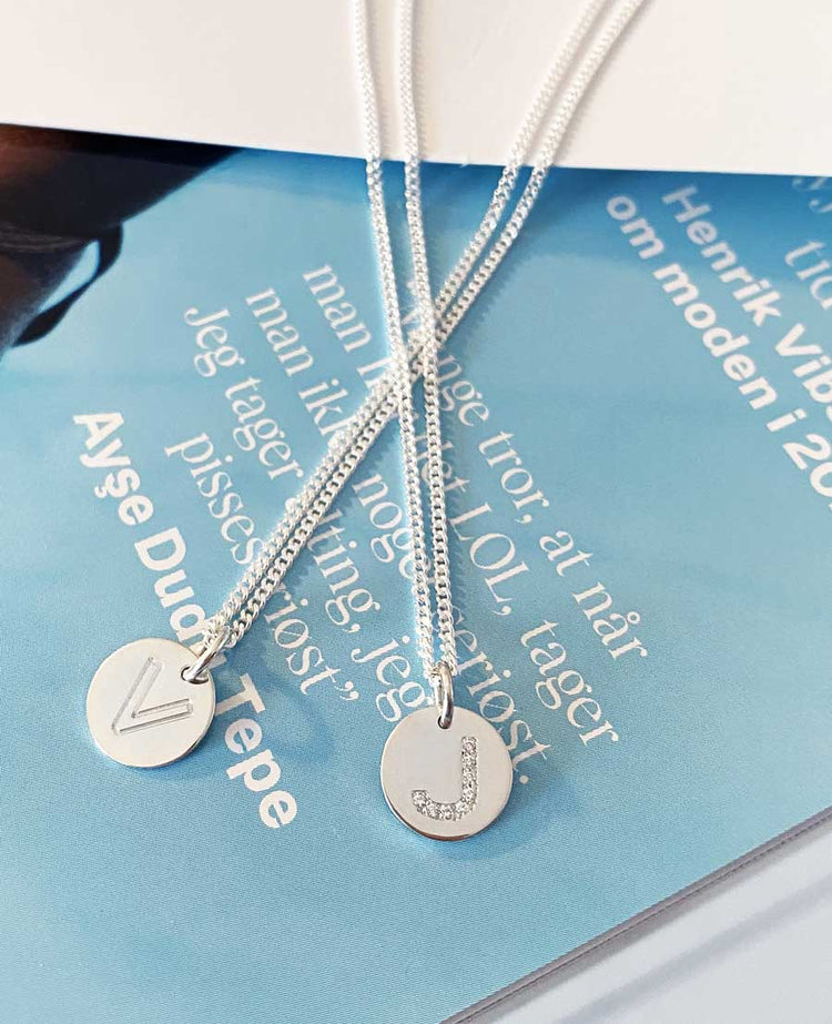 Två halsband med bokstavsberlocker i silver.