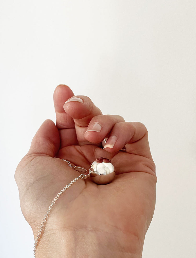 En hand som håller ett halsband med stor silverkula i kedja.