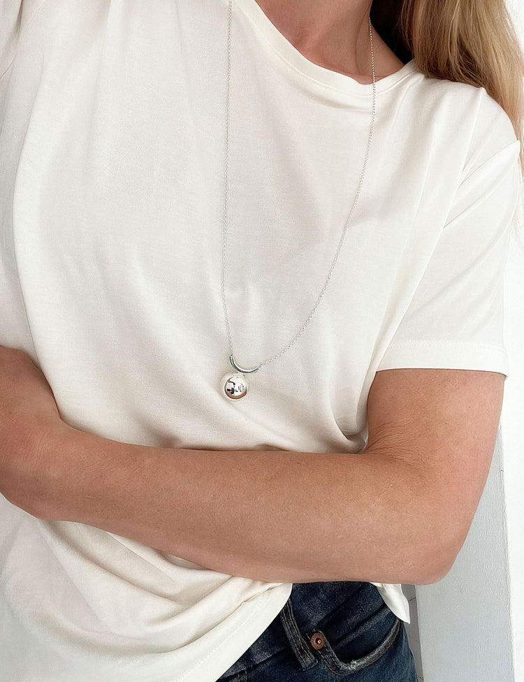 Tjej som bär ett långt silverhalsband med en stor kula.