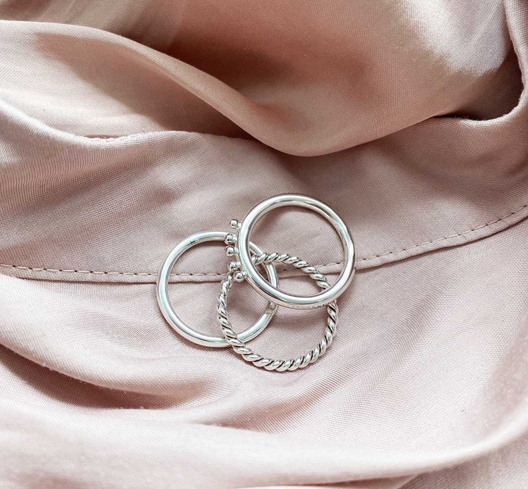 Tre smala silverringar som ligger på ett tyg.