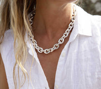 Tjej som bär ett chunky kedjehalsband i glänsande vitt silver. 