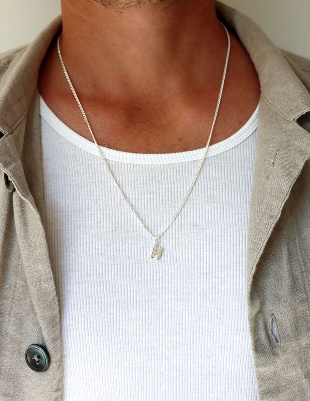 Man som bär ett längre halsband med kedja och bokstavsberlock i silver. 