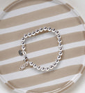 Armband med kulor i silver som har ställbar längd, placerat på ett randigt fat. 