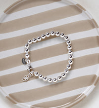Armband med kulor i silver som har ställbar längd, placerat på ett randigt fat. 